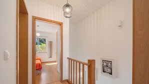 Un couloir doté d’un plancher en bois, d’une rambarde en bois, d’un luminaire suspendu et d’un tableau encadré accroché au mur.