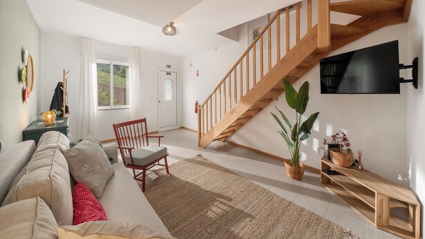 Un salon avec un escalier en bois, un canapé, un fauteuil, un téléviseur et une plante.