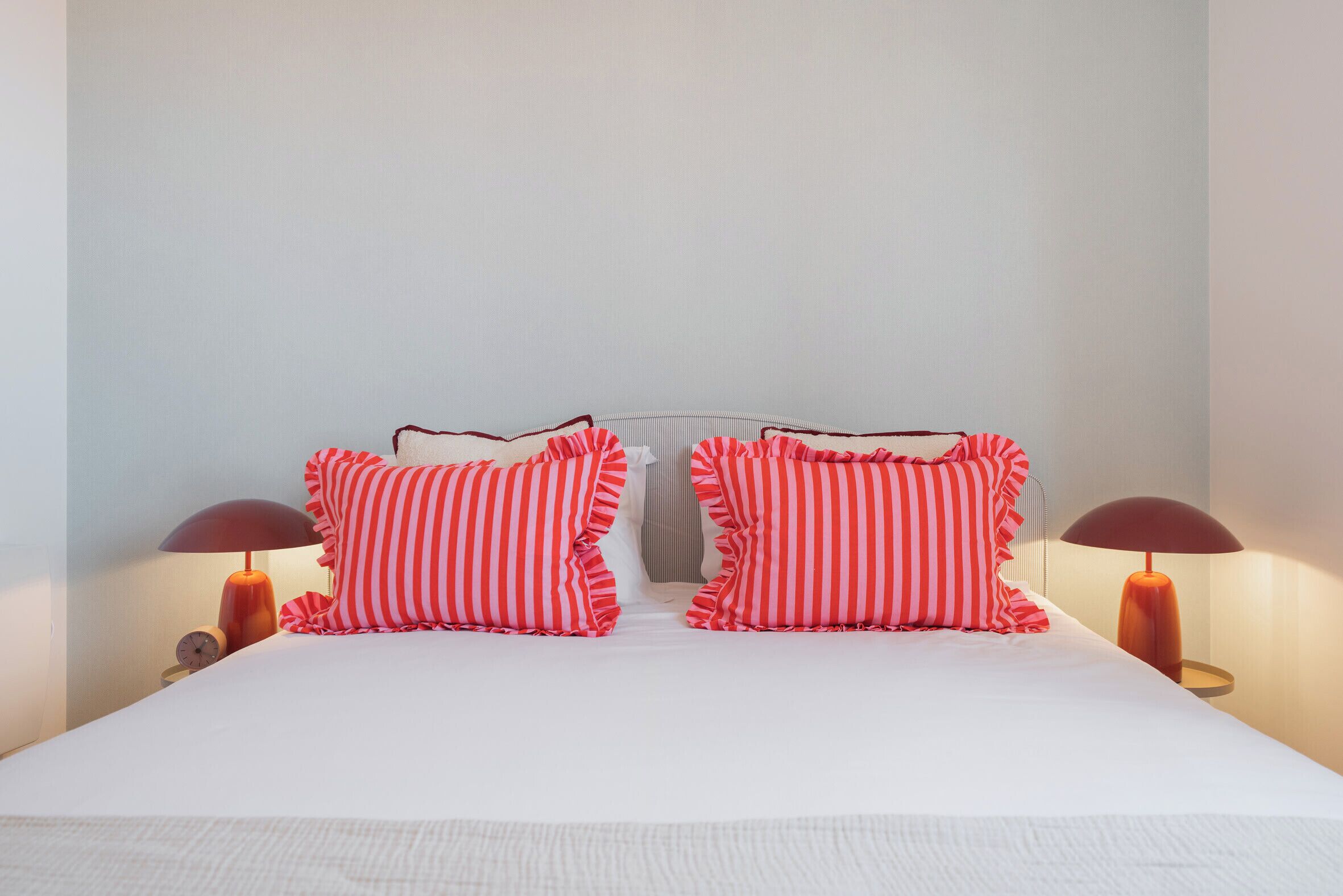 Un letto rifatto con cuscini a righe e due abat-jour.