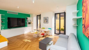 Un salon moderne comprenant un canapé, un téléviseur, un coin repas avec des chaises et un espace cuisine avec des placards.