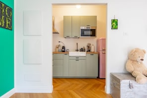A kitchen with light green cabinets, a white sink, and a pink refrigerator.