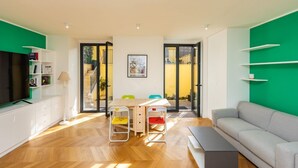Un salon moderne avec un canapé, une table à manger et des chaises. On y trouve également un téléviseur posé sur un meuble et une bibliothèque remplie de livres.