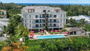 Un hotel de varios pisos con balcones, piscina y sombrillas rojas.