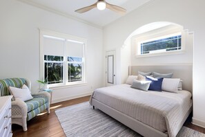 A bedroom with a large bed, a chair, a small table, a window, and a ceiling fan. - Pool Heated & Private, Close to Beach, Luxury Home (Holmes Beach)