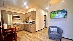 A modern kitchen with wooden cabinets, a dining table, and a gray armchair with a pillow. - Villa Hermosa- Guest Quarters (Prescott)