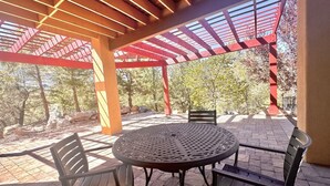 An outdoor patio with a round metal table and four chairs, surrounded by a red pergola structure. - Villa Hermosa- Guest Quarters (Prescott)