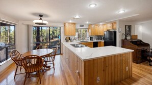 A modern kitchen with wooden cabinets, a large island, and a dining area with chairs. - Private - Amidst The Forest (Prescott)