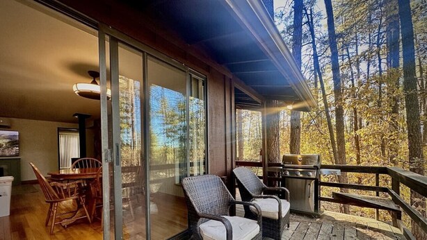 A wooden deck with wicker chairs and a grill, overlooking a forested area. - Private - Amidst The Forest (Prescott)