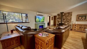 A living room with a brown leather sofa, a wooden coffee table, a fireplace, and a stone wall. - Private - Amidst The Forest (Prescott)