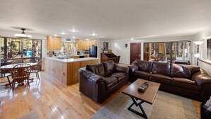 A spacious living area with a large brown leather sofa, wooden dining table, and a kitchen with wooden cabinets and a central island. - Private - Amidst The Forest (Prescott)
