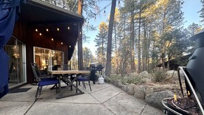 A patio with a table and chairs, a barbecue grill, and a building with large windows. - Morning Bliss - Multi Family & Couples (Prescott)