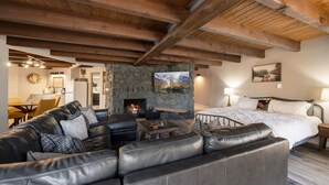 A cozy living room with a stone fireplace, leather sofas, and a bed with a nightstand. - Morning Bliss - Multi Family & Couples (Prescott)