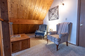 A cozy room with wooden ceiling beams, a blue armchair, a striped armchair, and a small wooden table. - Peakview Lodge - Wood Burning Stove-Gorgeous Views (Prescott)