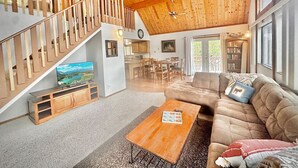 A spacious living area with a wooden staircase, a television on a wooden console, a sofa, and a dining area in the background. - NEW - Peakview Lodge - Fireplace- Views (Prescott)