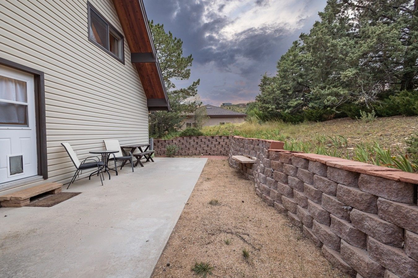 A patio with outdoor furniture, a stone retaining wall, and a house with siding and a window.