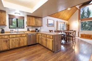 A kitchen with wooden cabinets, a dishwasher, and a dining area with a table and chairs. - Peakview Lodge - Wood Burning Stove-Gorgeous Views (Prescott)