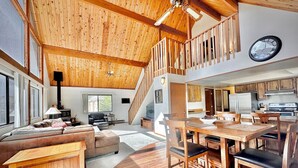 A spacious living area with a wooden ceiling, a dining table with chairs, a sofa, and a staircase leading to an upper level. - NEW - Peakview Lodge - Fireplace- Views (Prescott)