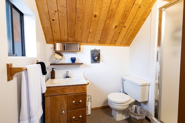 A bathroom with a wooden ceiling, a white sink, a toilet, and a towel rack.