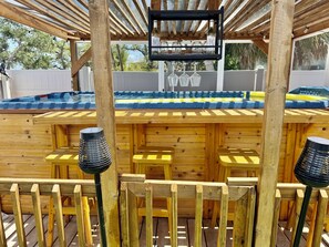 Una terraza de madera con barra, asientos exteriores y un jacuzzi.