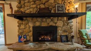 A stone fireplace with a black surround, a framed picture above it, and a green chair to the right.