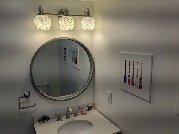 Une salle de bain avec un miroir rond, trois appliques murales, un lavabo et un tableau représentant des battes de baseball.