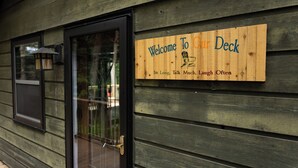 A wooden sign with the text "Welcome to Our Deck" and a message "Sit Long, Talk Much, Laugh Often" on a building's exterior wall.