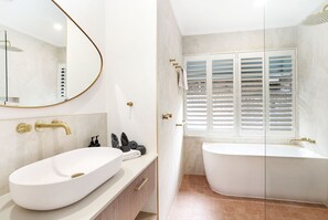 Ein Badezimmer mit einem weißen Waschbecken, goldenen Armaturen, einem großen Spiegel und einer Badewanne.