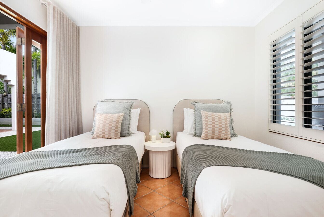 Une chambre d’hôtel avec deux lits simples, une petite table ronde avec une lampe et une fenêtre avec des stores.