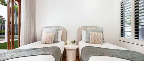 Une chambre d’hôtel avec deux lits simples, une petite table ronde avec une lampe et une fenêtre avec des stores.