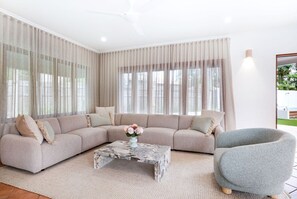 Ein modernes Wohnzimmer mit einem beigefarbenen Ecksofa, einem Marmor-Couchtisch und einem grauen Sessel.