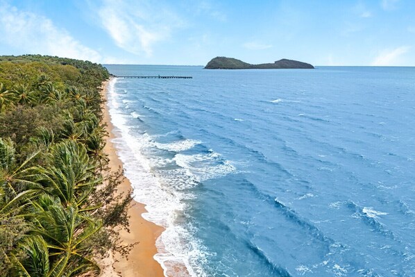 Una playa con palmeras, un muelle y islas a lo lejos.