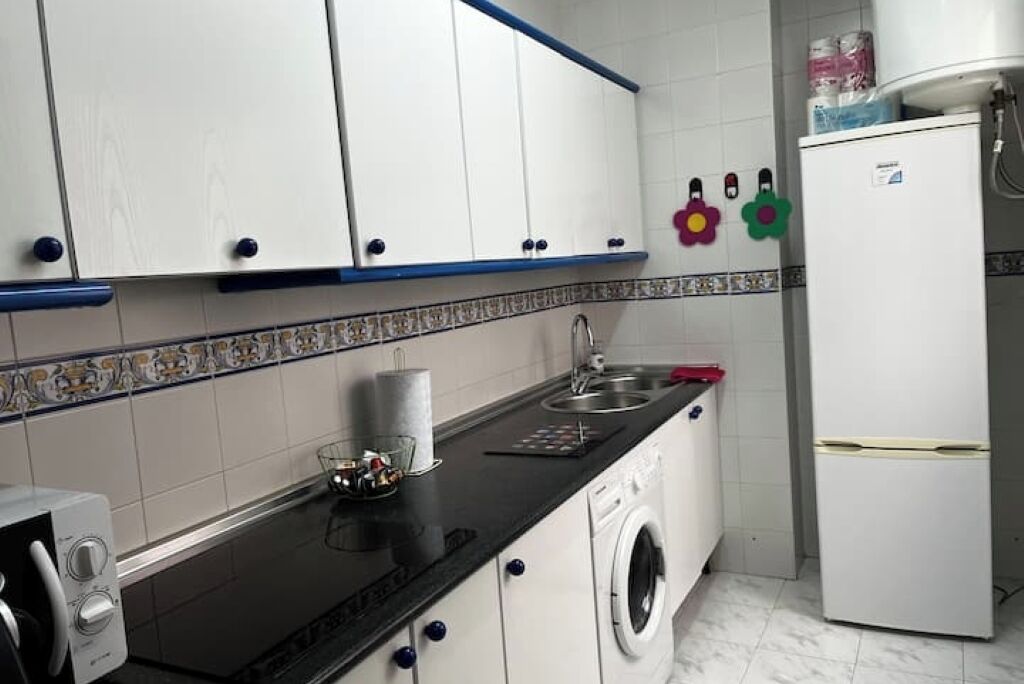 A compact kitchen with white cabinets, a black countertop, a washing machine, and a refrigerator.