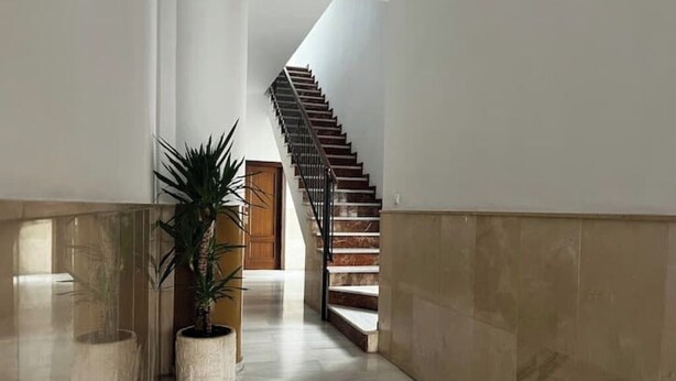 A hallway with a marble floor, a potted plant, and a staircase leading to a wooden door. - Apartment in Centro de Ronda, dream city (Ronda)