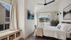 A bedroom with a bed, a TV, a ceiling fan, a window with curtains, a view of the outdoors, and a patterned rug. - 4\2.5+ LAKE HOUSE — Fish & Swim @DOCK; LakeMat; Kayak; PaddleBoard; King & Queen (Montgomery)