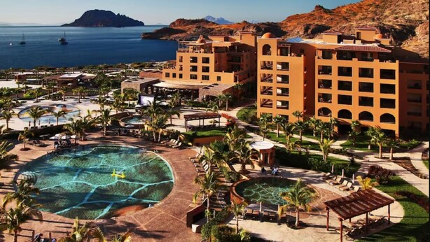 Un resort con varias piscinas, un edificio grande con balcones y vista al mar.