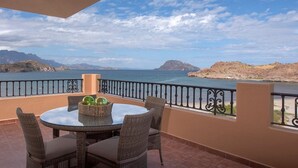 Un balcón con una mesa redonda y sillas de mimbre, con vistas a un paisaje costero con montañas y una masa de agua.