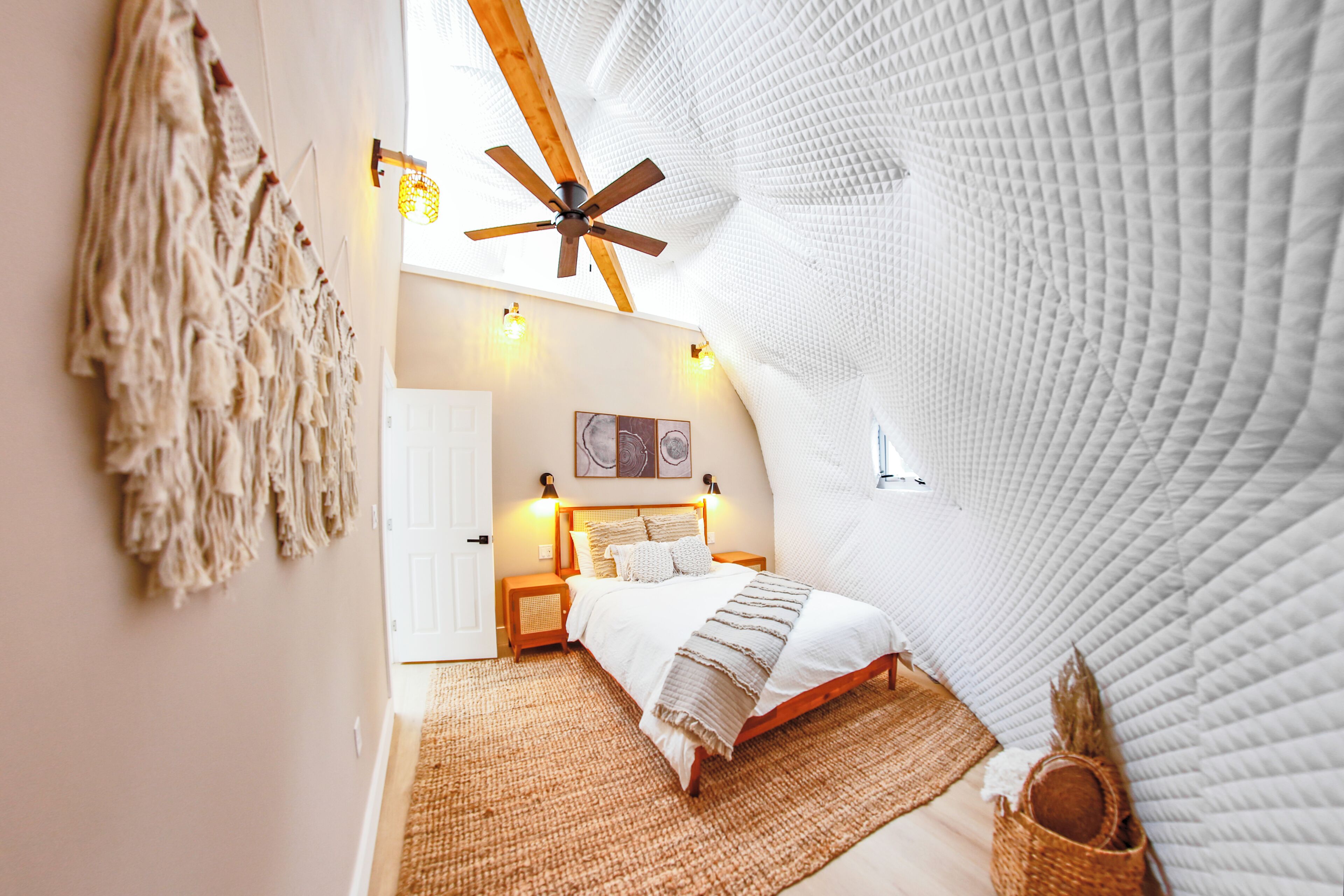 Ein gemütliches Schlafzimmer mit schrägen Wänden, einem hölzernen Bett, einer Wanddekoration aus Makramee und einem Deckenventilator.