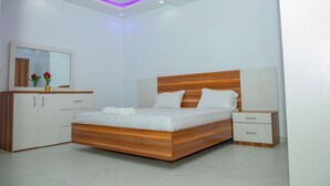 A modern bedroom with a wooden bed, white bedside tables, and a built-in wardrobe. - Le Tamarin (Dakar)