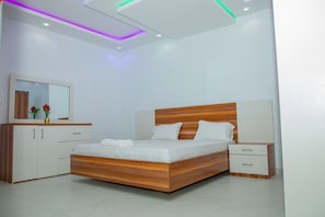 A modern bedroom with a wooden bed, white bedside tables, and a built-in wardrobe. - Le Tamarin (Dakar)