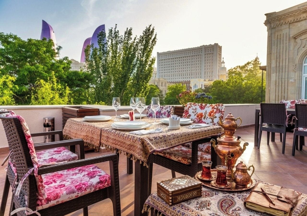 Un área de comedor en la azotea con una mesa preparada para cuatro personas, rodeada de sillas de mimbre con tapicería floral.