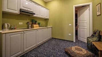 Una cocina compacta con armarios blancos, estufa integrada y piso estampado. Una puerta conduce a una sala de estar con alfombra estampada y un banco.