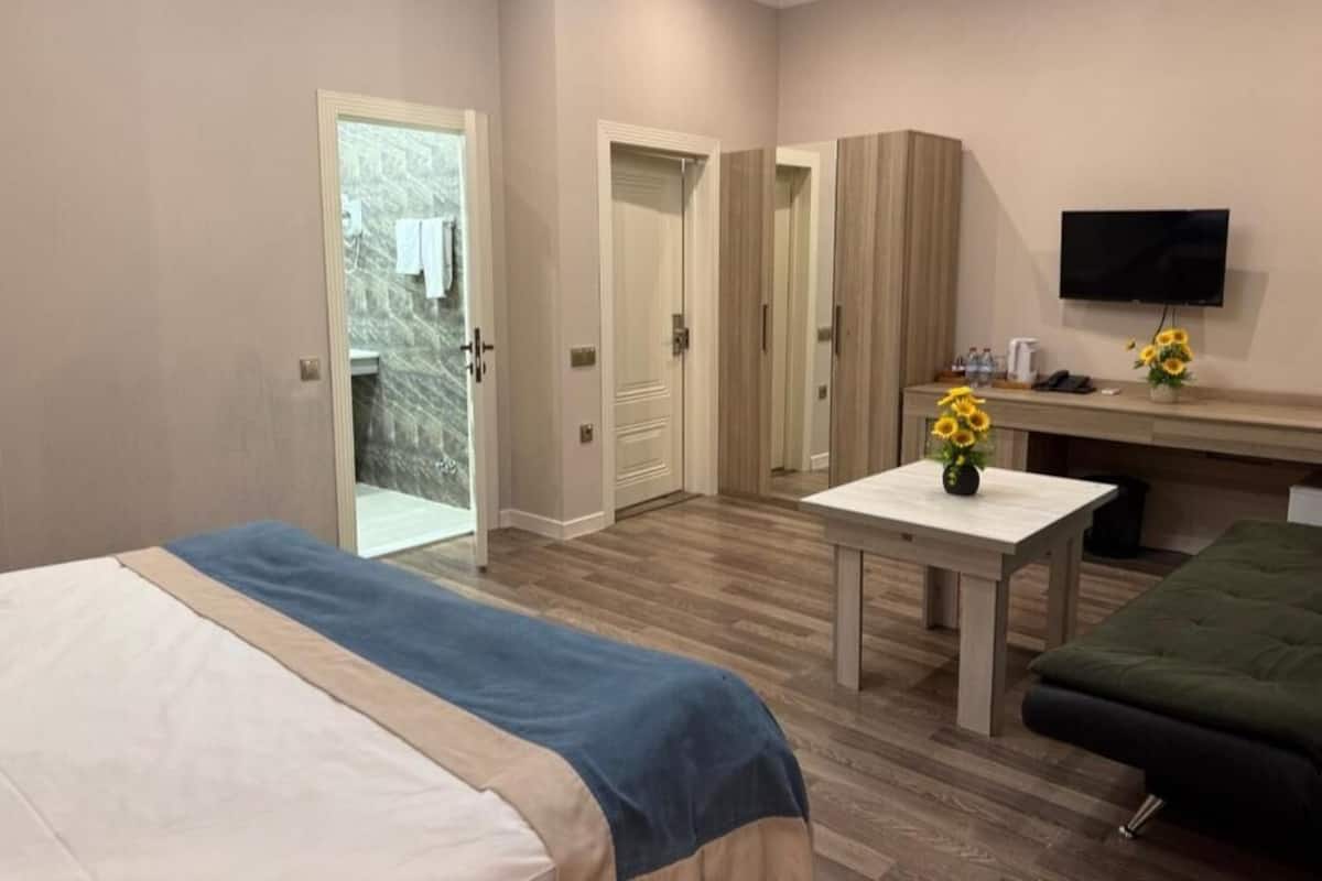 A hotel room with two beds, a desk, a TV, and a bathroom visible through an open door.