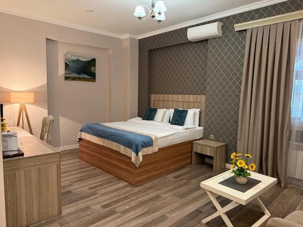A hotel room with a wooden bed, a desk with a lamp, a small table with a vase of flowers, and a window with curtains.