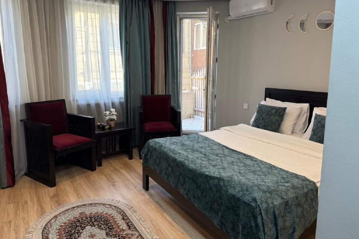 A hotel room with a bed, two chairs, a small table, and a view of the outside.