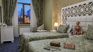 Habitación de hotel con dos camas, vista a la ciudad, un cabecero decorativo y una mesita de noche con lámpara.