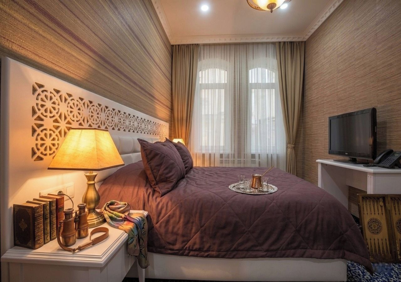 A hotel room with a bed, bedside table, lamp, books, and a television.
