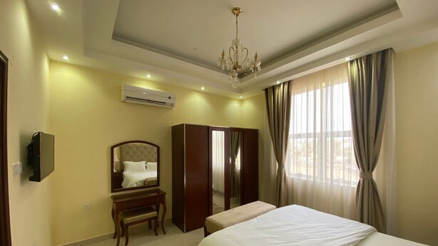 A hotel room with a bed, a wardrobe, a vanity with a mirror, an air conditioning unit, and a chandelier. - Very nice and relaxing (Salalah)