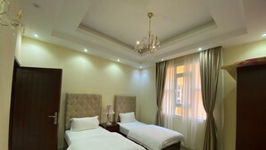 A hotel room with two beds, a chandelier, a wooden door, and a window with curtains. - Very nice and relaxing (Salalah)