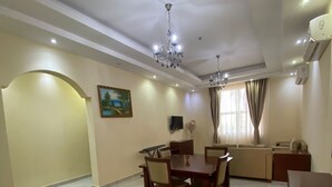 A spacious living room with a dining area, a sofa set, a TV mounted on the wall, and a chandelier. - Very nice and relaxing (Salalah)