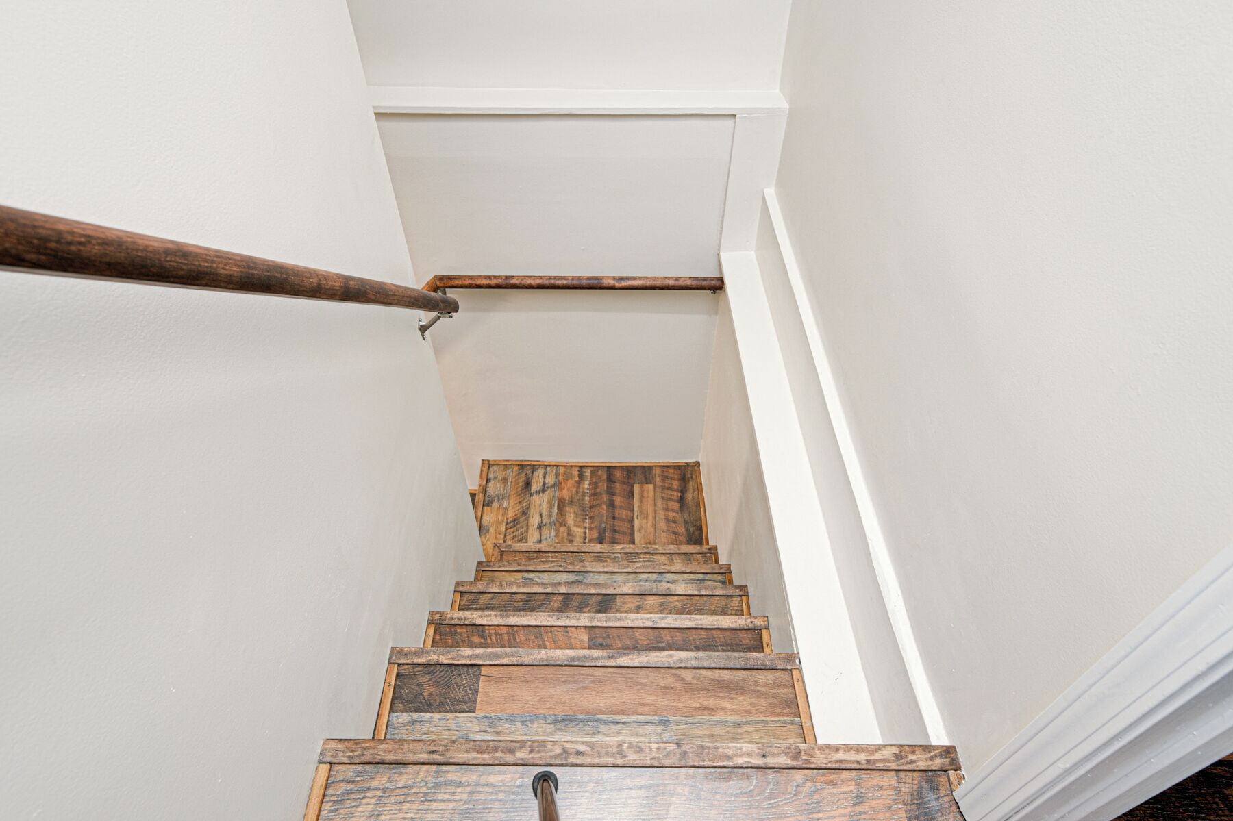A wooden staircase with a handrail and white walls.